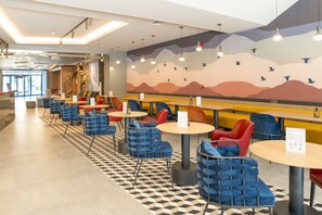 A modern cafe with blue and red chairs, checkered flooring, and a mural of birds on the wall. - Novotel Gaziantep (Gaziantep)