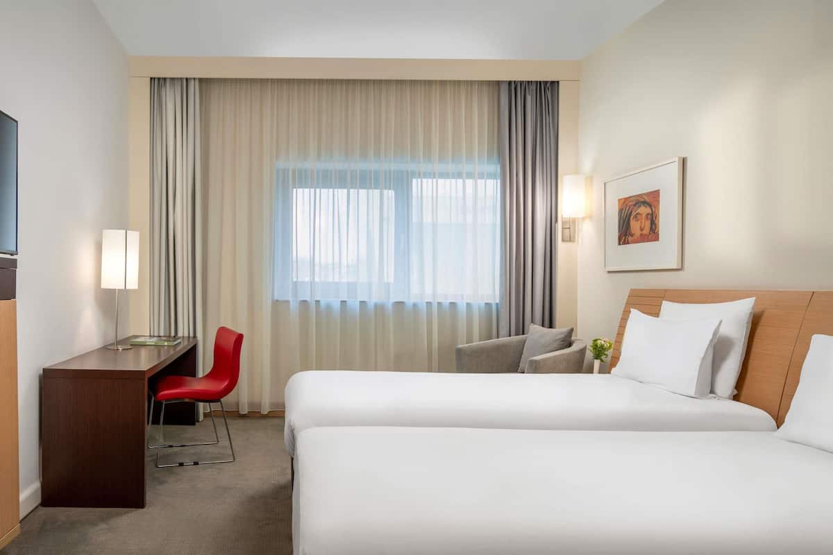 A hotel room with two beds, a desk, a chair, and a large window with curtains.
