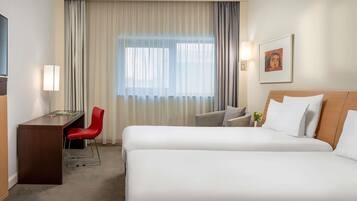 Habitación de hotel con dos camas, un escritorio, una silla y un ventanal con cortinas.