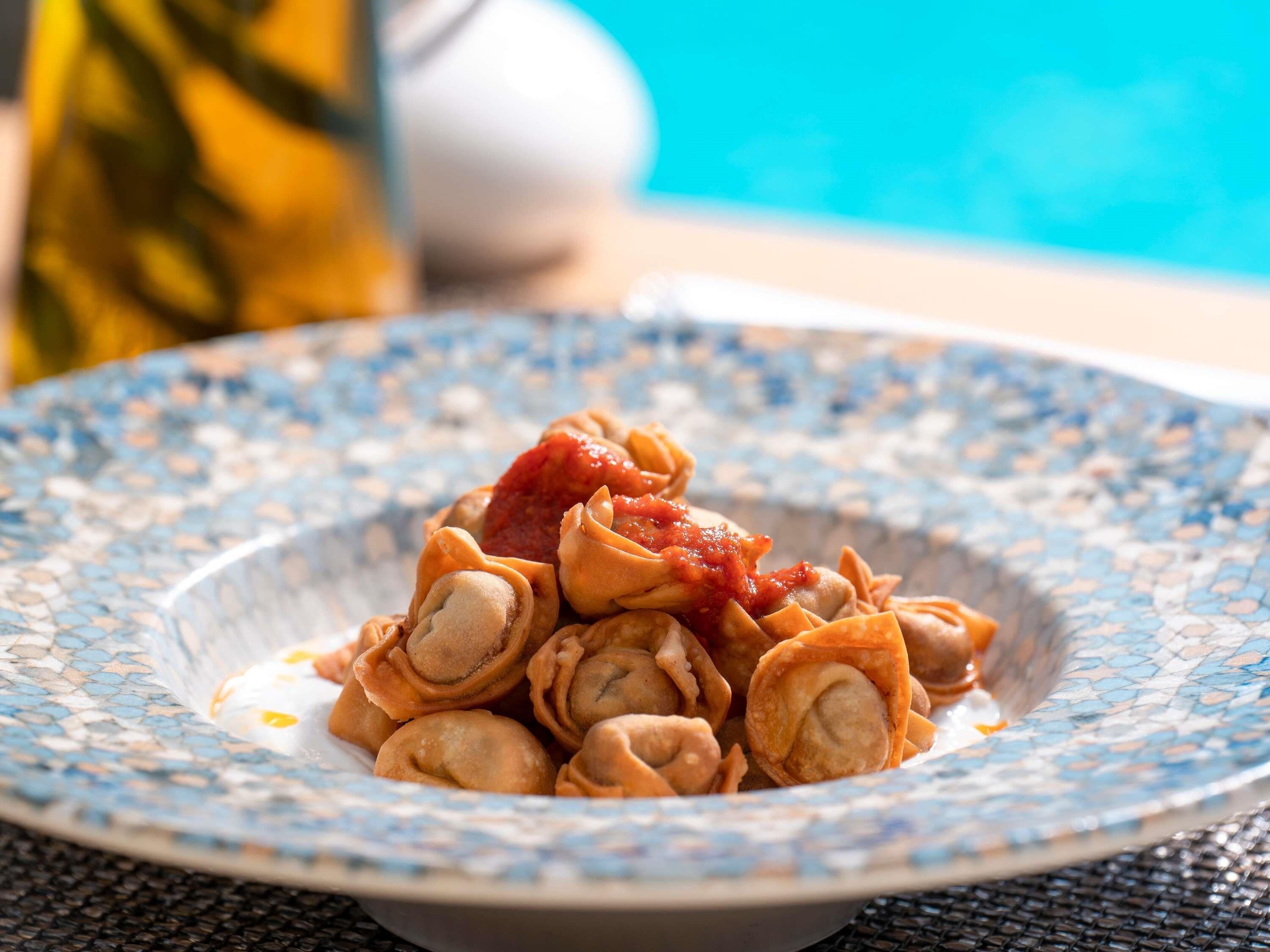 A plate of ravioli with tomato sauce on a blue and white patterned plate.