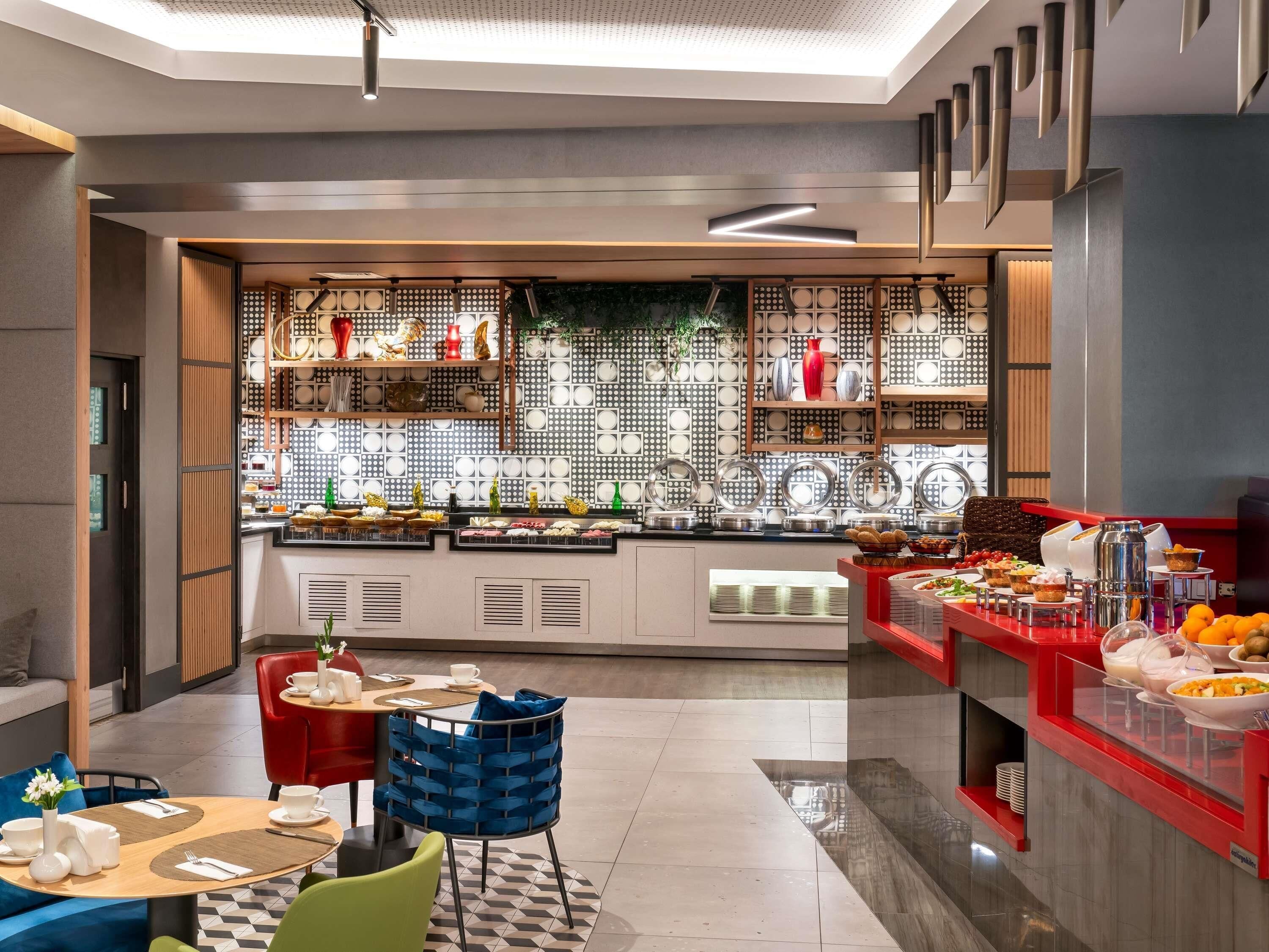Un área de desayuno moderna con mesas de buffet, distribución de asientos y una pared decorativa con paneles estampados.