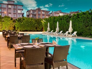 A poolside dining area with tables set for two, lounge chairs, and umbrellas. - Novotel Gaziantep (Gaziantep)
