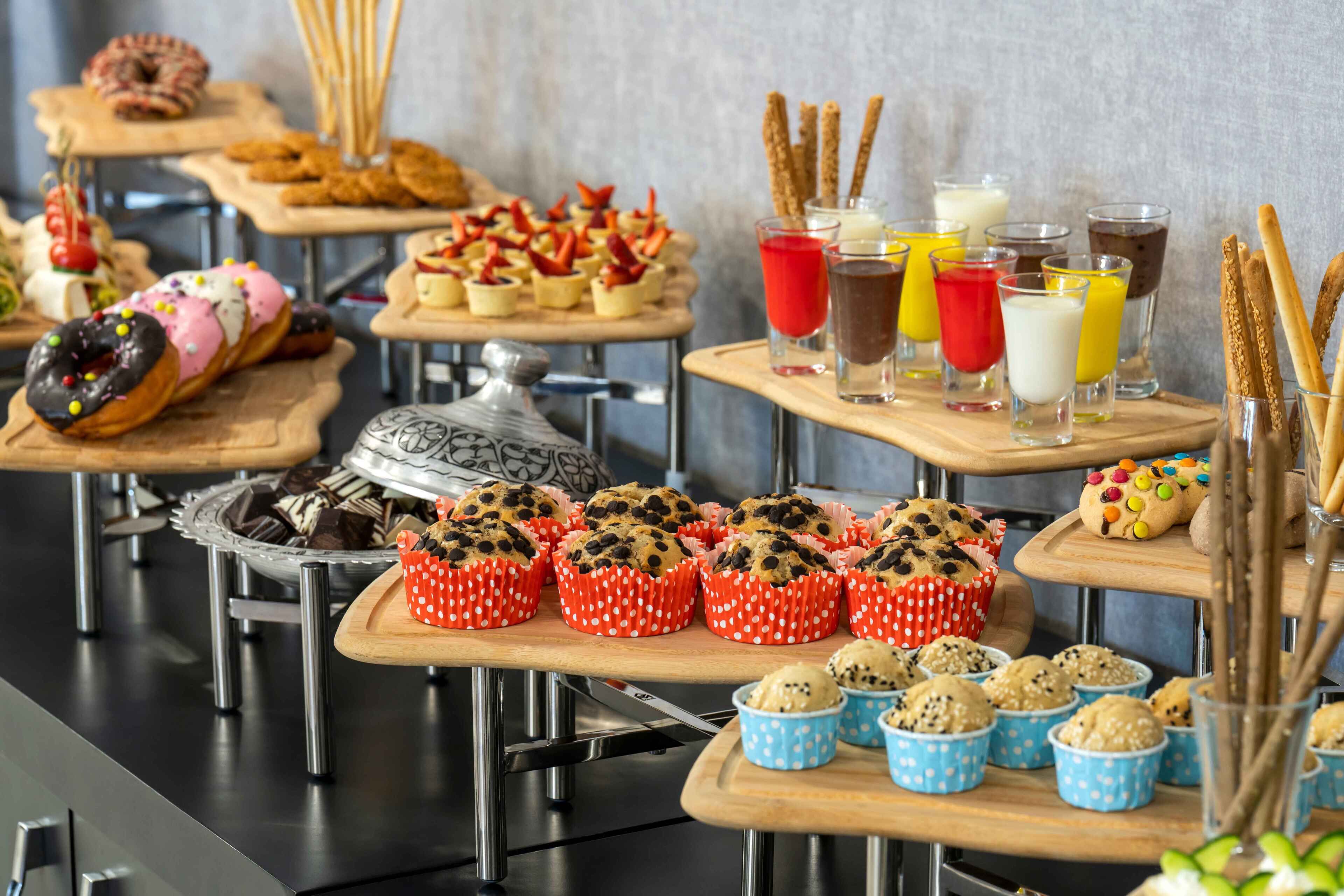 A buffet with various baked goods, including muffins and pastries, and a selection of colorful beverages.