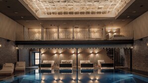 Una piscina interior moderna con sillones de descanso y un diseño de techo original.