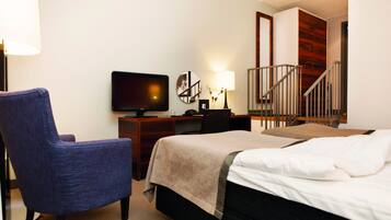 A hotel room with a bed, a desk with a television, a chair, a lamp, and a staircase.