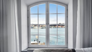 Una habitación con un amplio ventanal arqueado con vistas a un puerto deportivo con barcos y edificios.