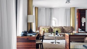 Quarto de hotel moderno com escrivaninha de madeira, mesa de centro redonda, sofá com almofadas e um espelho grande.