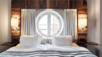 A bedroom with a large round window, wooden paneling on the walls, two bedside tables with lamps, and a bed with white bedding.