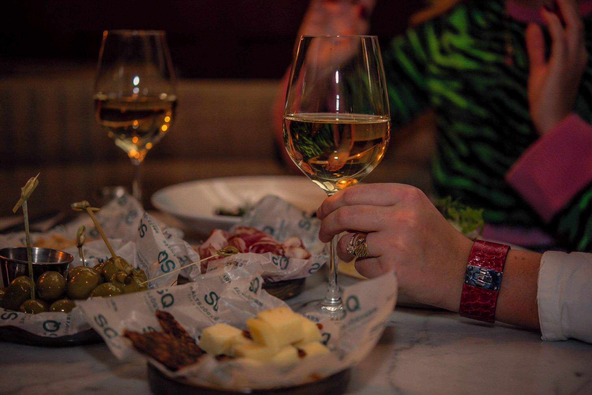 Ein Tisch mit einem Glas Weißwein, Oliven und Käse.
