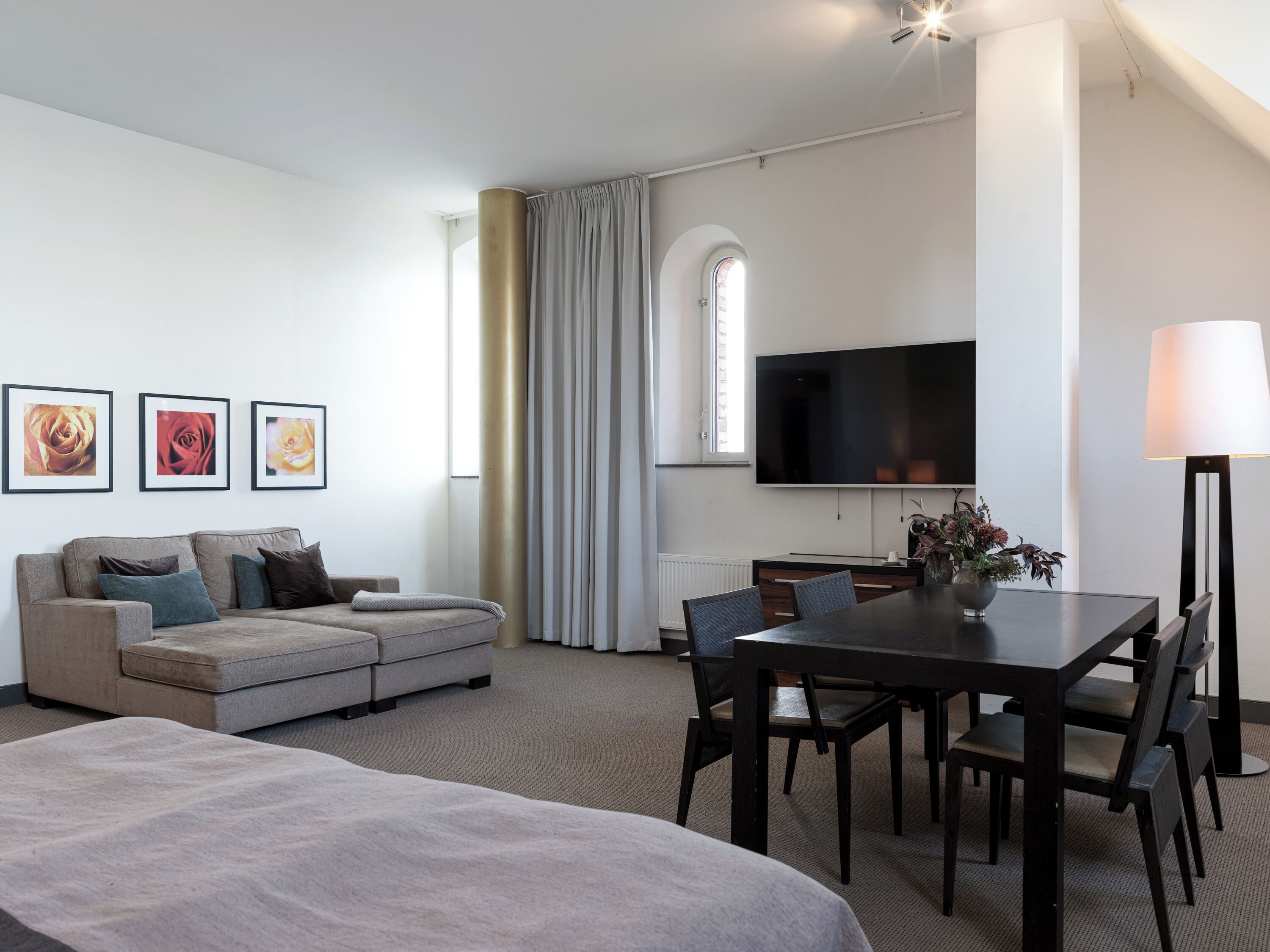 Et moderne hotelværelse med en sofa, et spisebord med stole, et fladskærms-tv og en lampe.