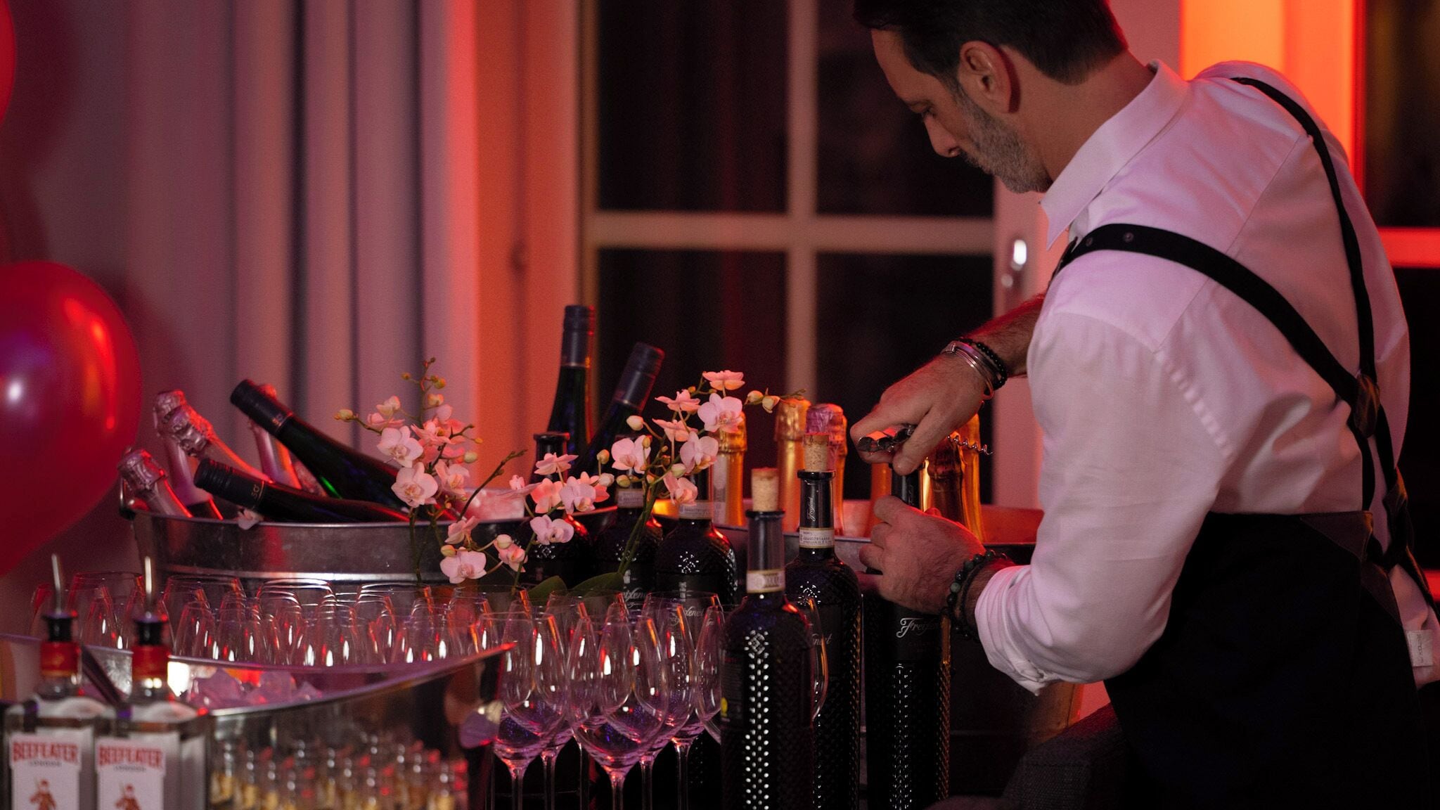 Un barman preparant còctels al bar, amb ampolles i vasos.