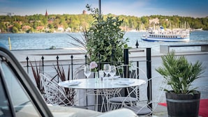 Un restaurante frente al agua con terraza, vistas al mar y un barco al fondo.
