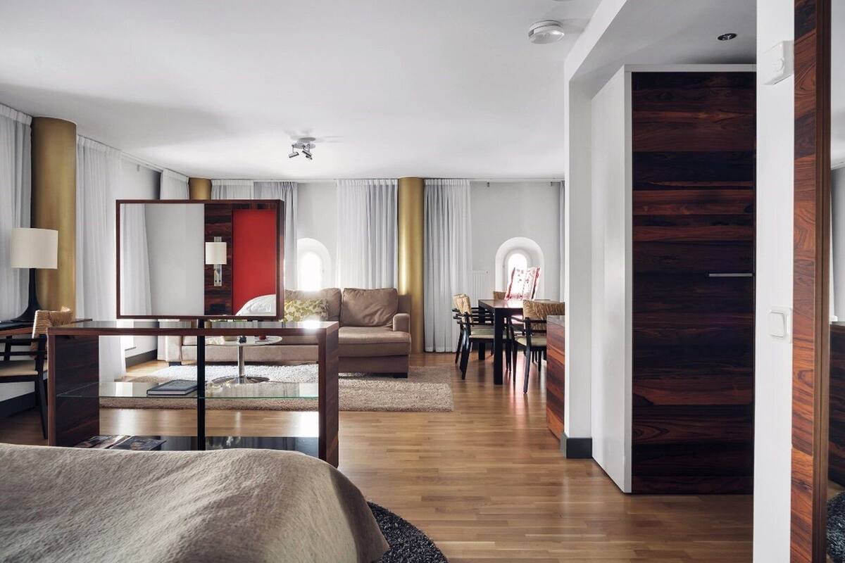 Una habitación de hotel moderna con una cama grande, una zona de estar con sofá y sillones, una mesa de comedor con sillas y una pared de acento de madera.