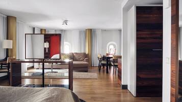Una habitación de hotel moderna con una cama grande, una zona de estar con sofá y sillones, una mesa de comedor con sillas y una pared de acento de madera.