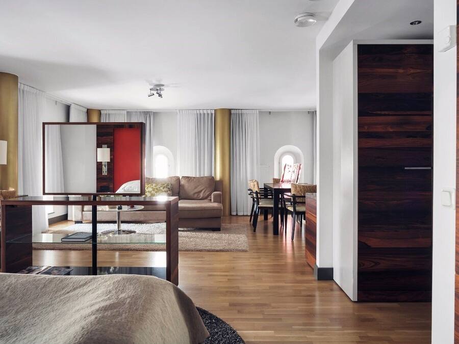 Una habitación de hotel moderna con una cama grande, una zona de estar con sofá y sillones, una mesa de comedor con sillas y una pared de acento de madera.