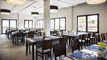 En rummelig restaurant med flere borde og stole, store vinduer og moderne hængelamper.