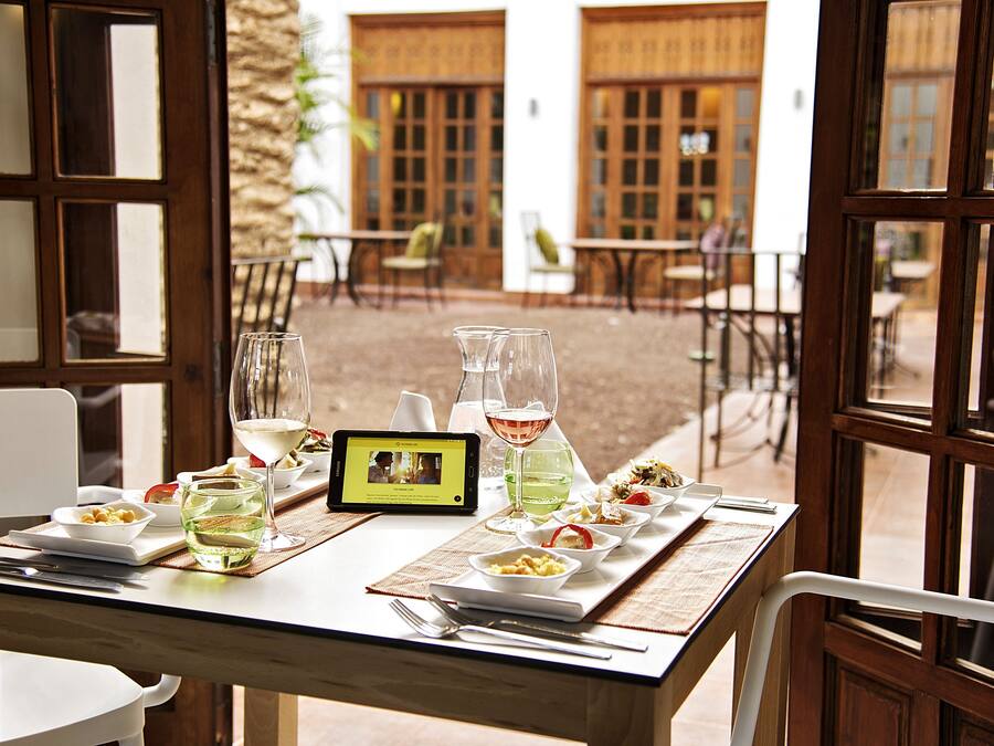 A dining table set with plates, glasses, and a tablet displaying a video.