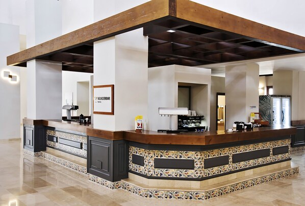 A spacious lobby with a central reception desk, a coffee machine, and a framed sign.