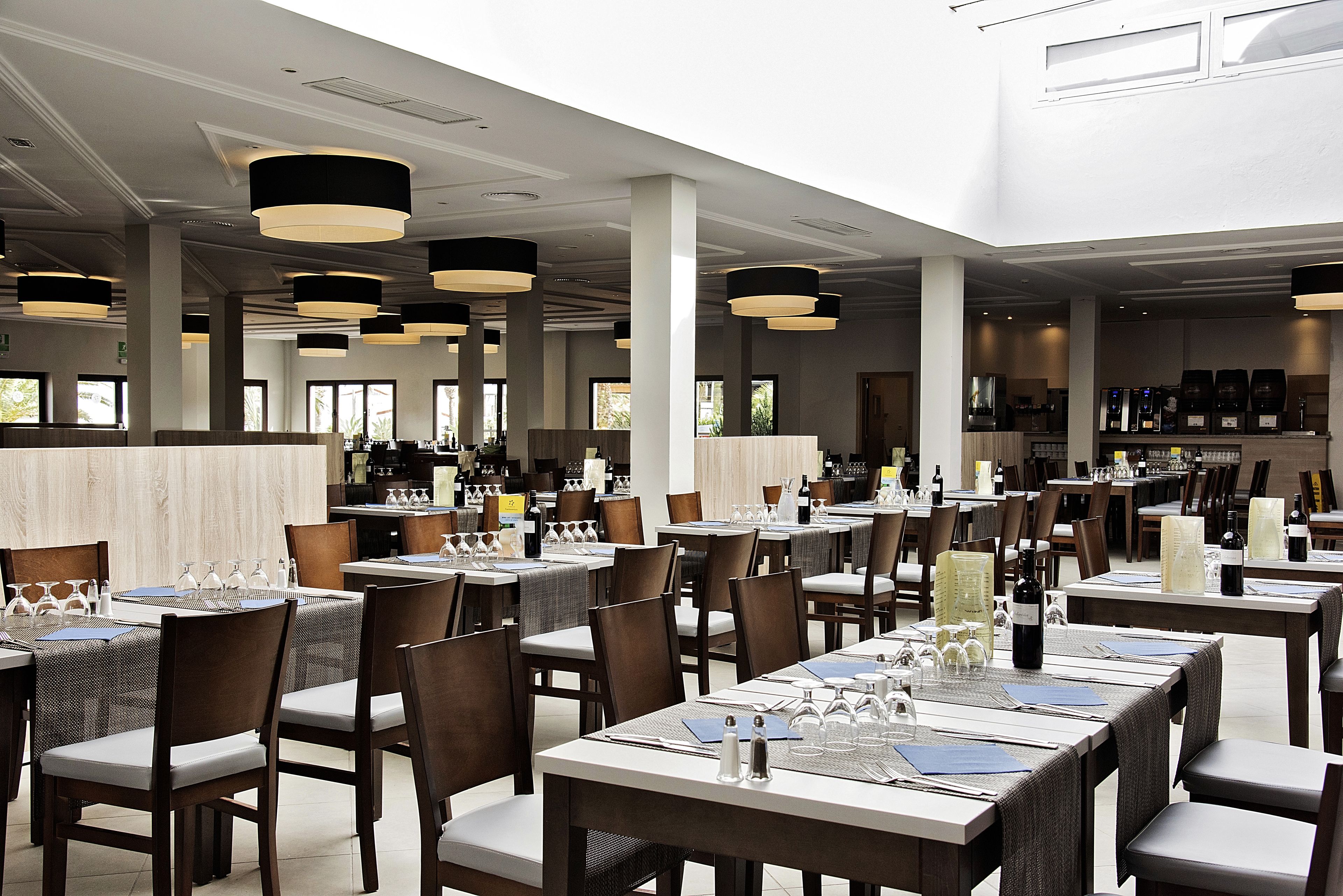 Een ruim restaurant met meerdere eettafels, stoelen en hangende吊灯.