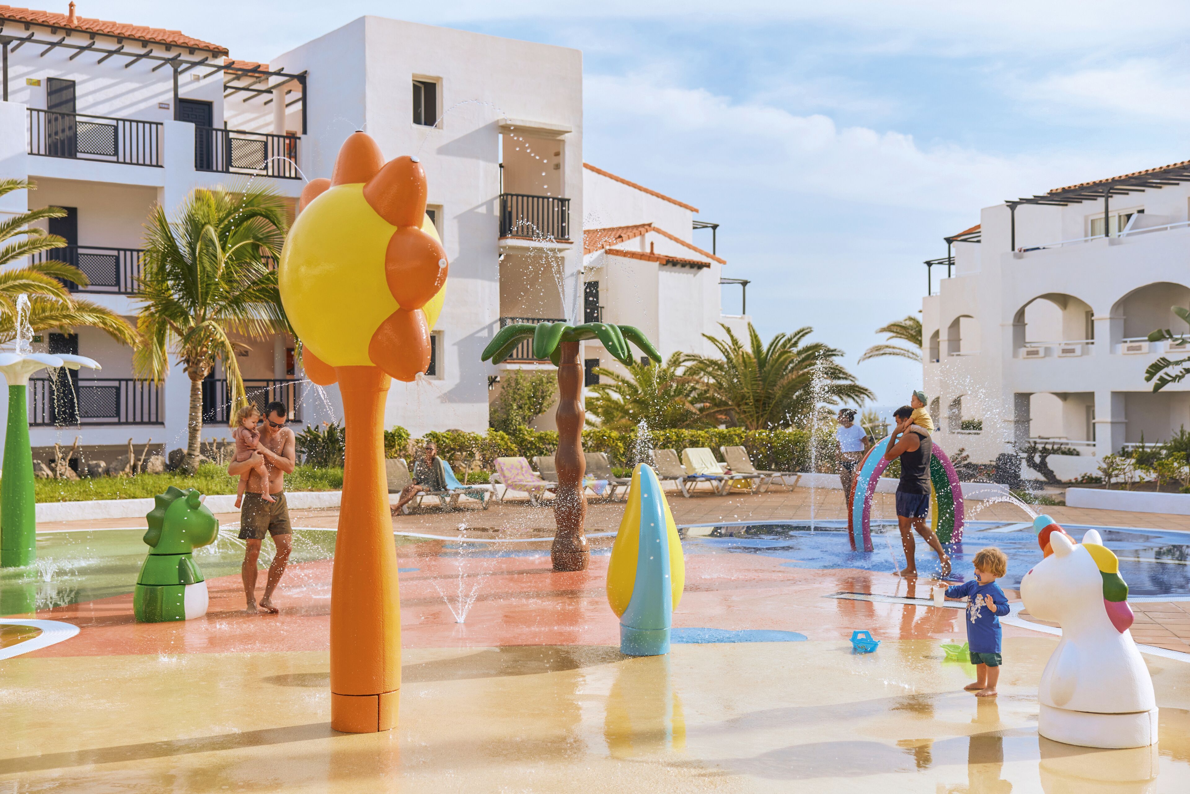 A water park with various water features and pools, surrounded by buildings with balconies and palm trees.