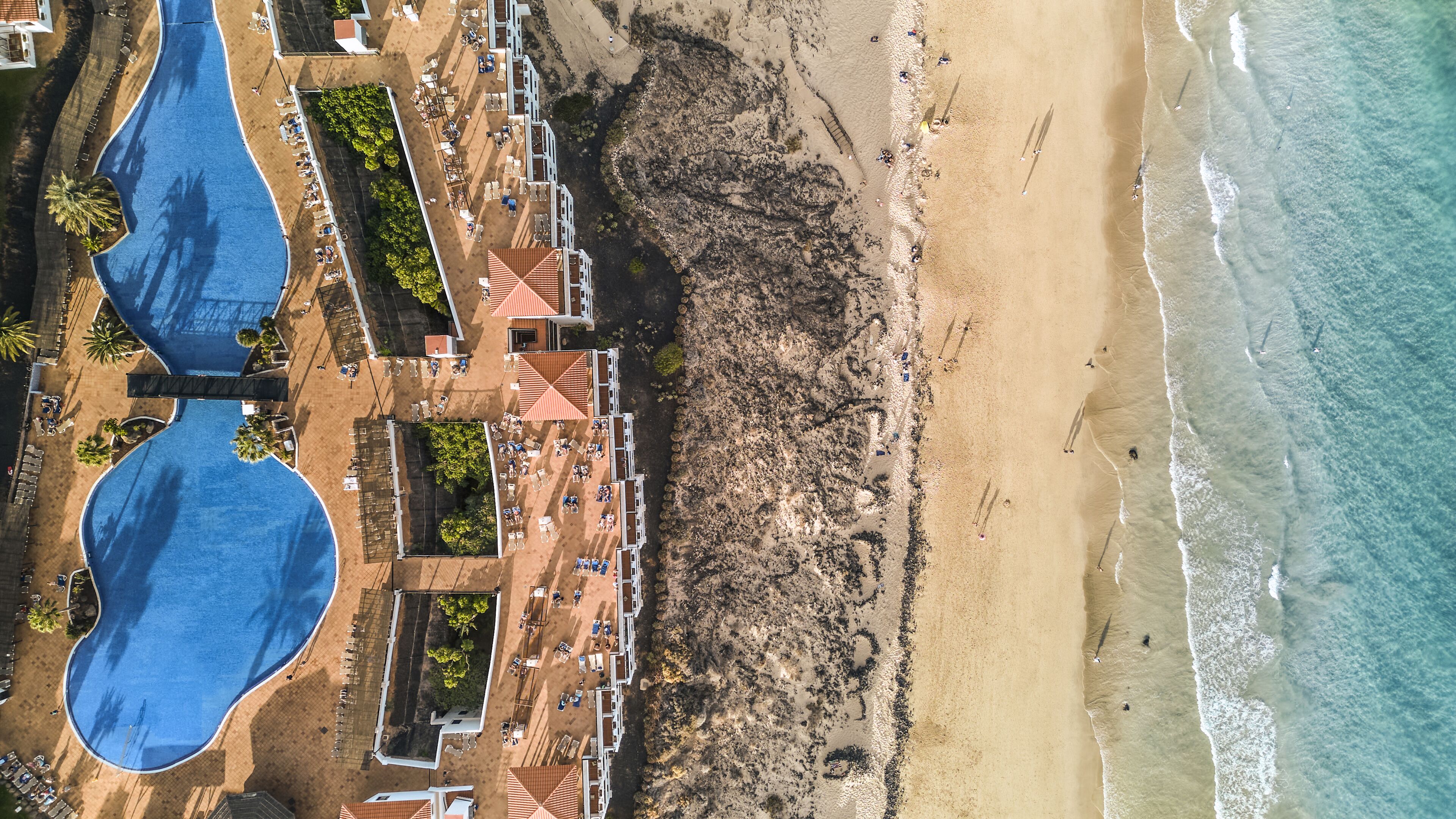An aerial view of a resort with two large swimming pools, a beach area, and a rocky shoreline.