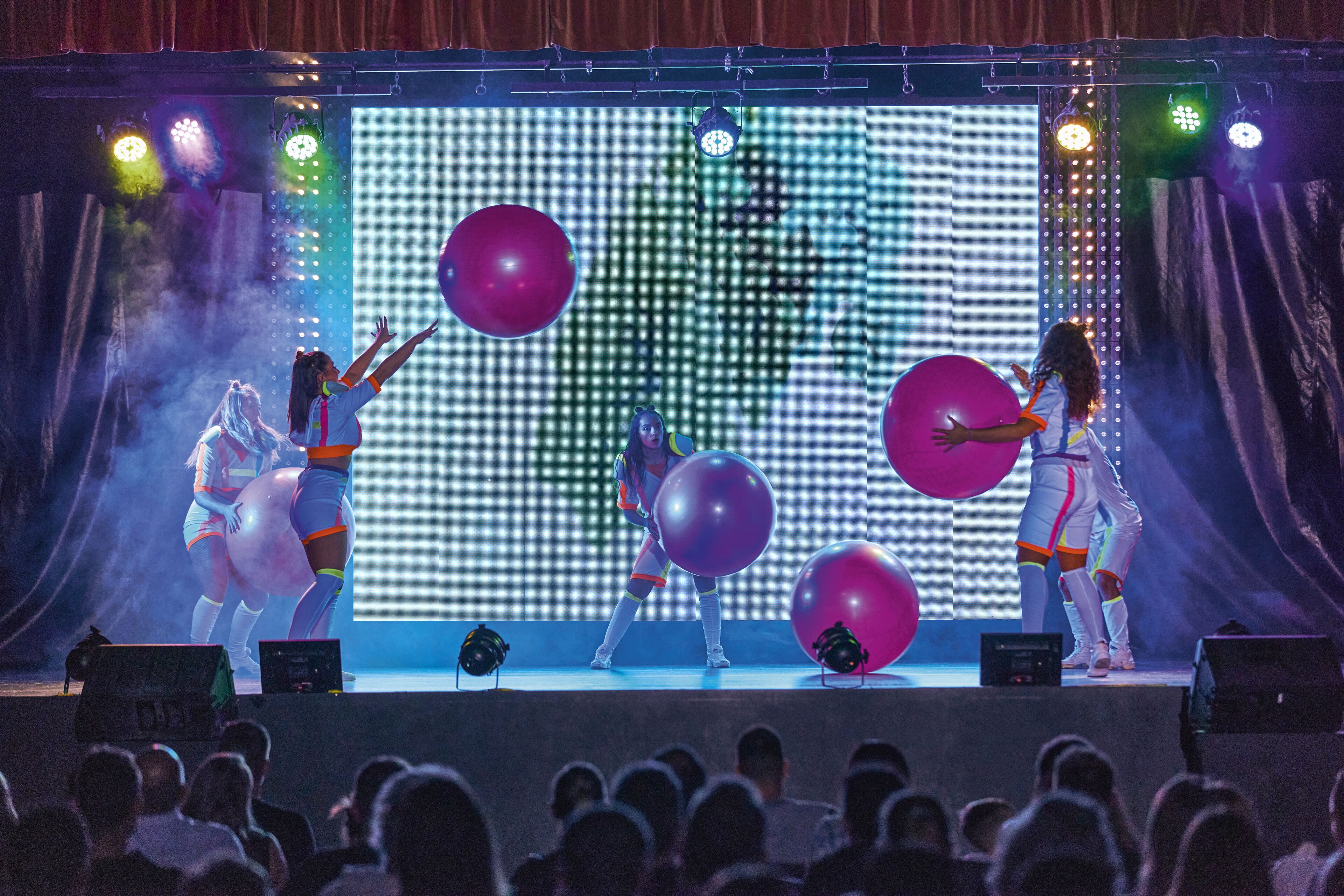 Un escenario con artistas, una pantalla grande y una multitud.