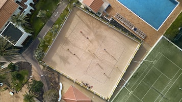 Luchtbeeld van een strand met een volleybalveld, een zwembad en omliggende gebouwen.