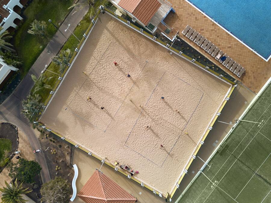 Luchtbeeld van een strand met een volleybalveld, een zwembad en omliggende gebouwen.