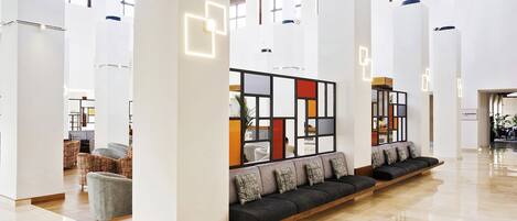 Um hall moderno com um sofá comprido, tetos altos e piso lustroso.