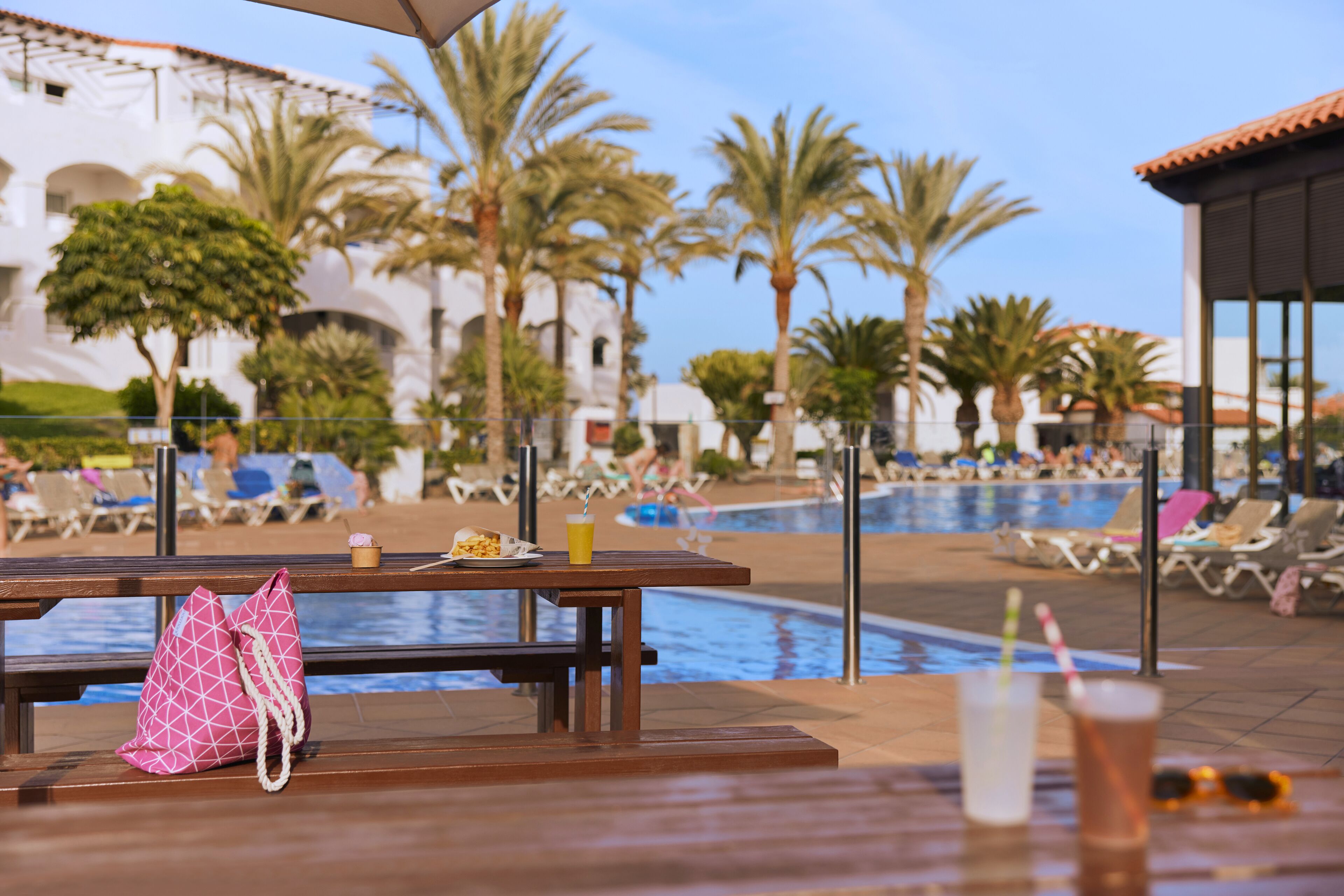 A poolside area with lounge chairs, a table with a drink, and a pink bag.