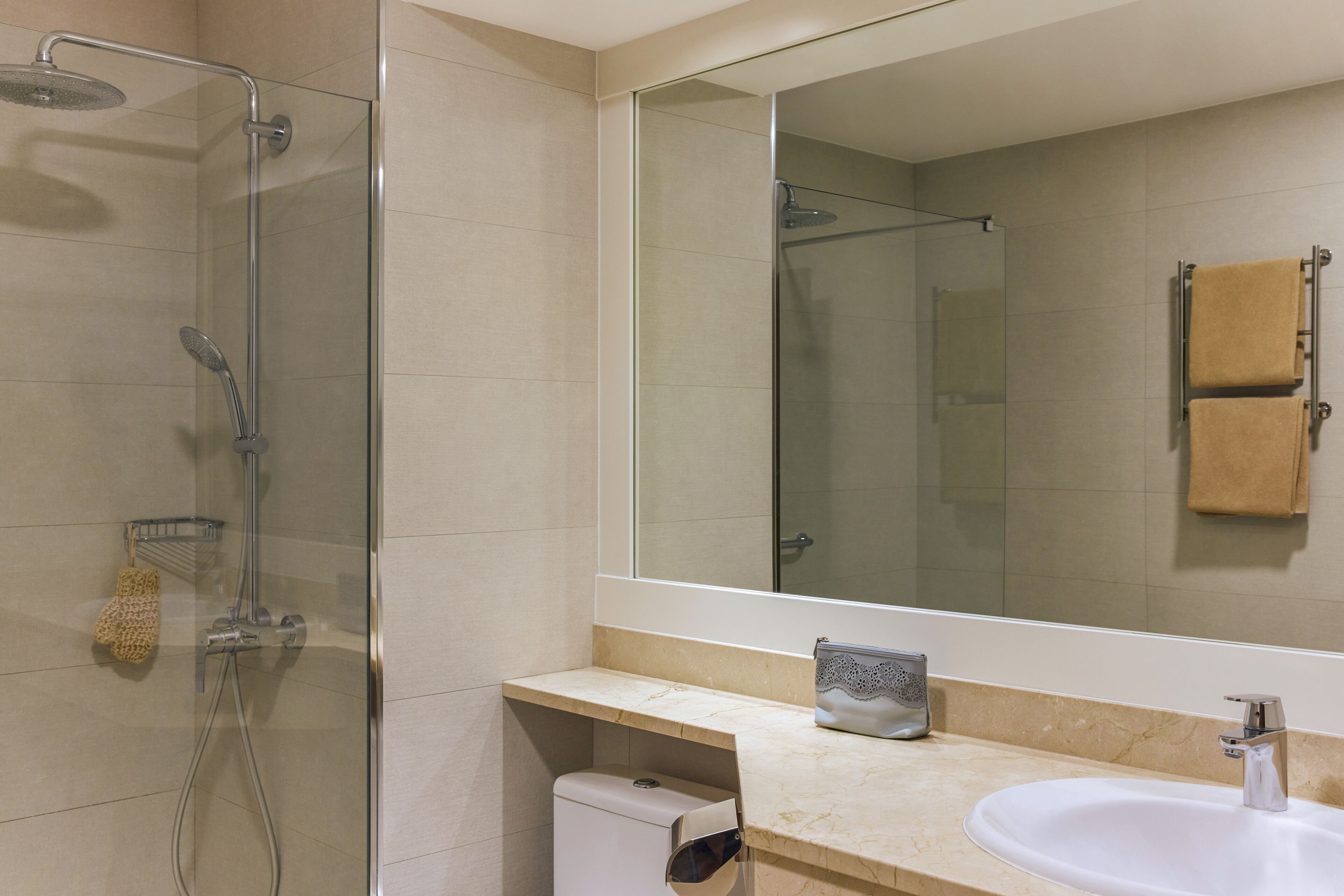 A modern bathroom with a glass-enclosed shower, a white sink, and a large mirror.