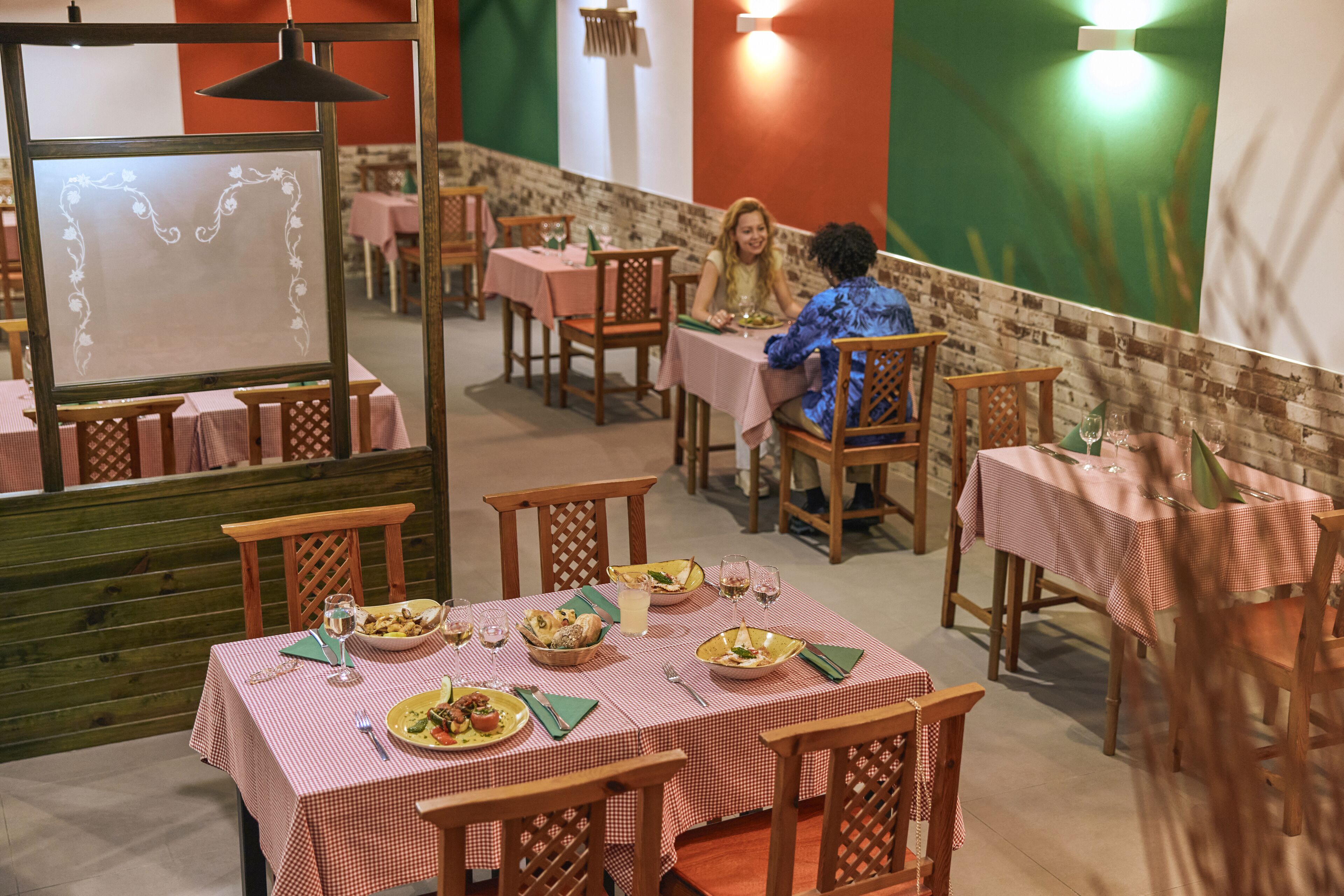 A restaurant with checkered tablecloths, wooden chairs, and a brick wall.