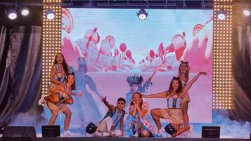 Un escenario con artistas, una pantalla grande e iluminación escénica.