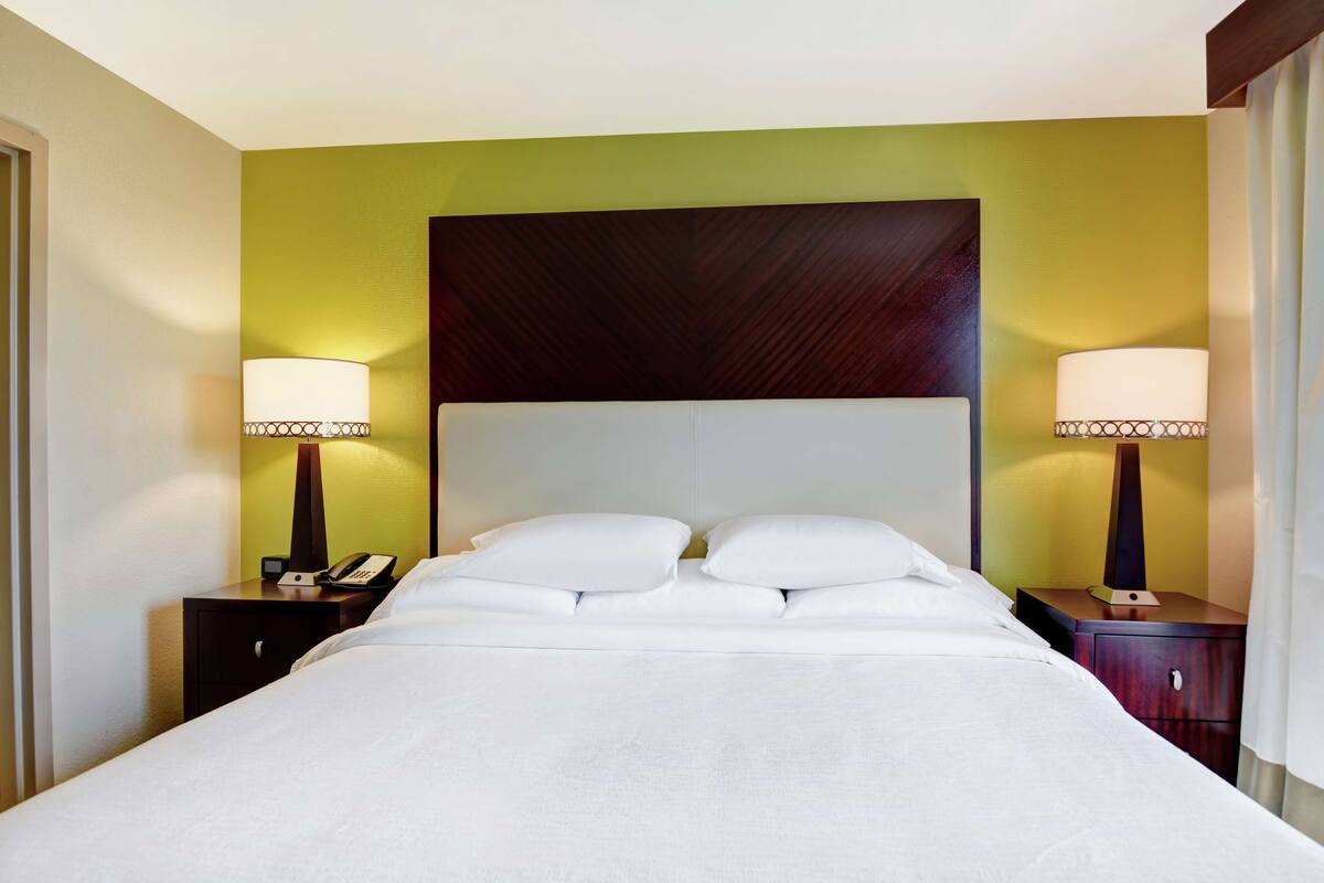 Habitación de hotel con una cama grande, dos mesitas de noche con lámparas y un cabecero de madera oscura.