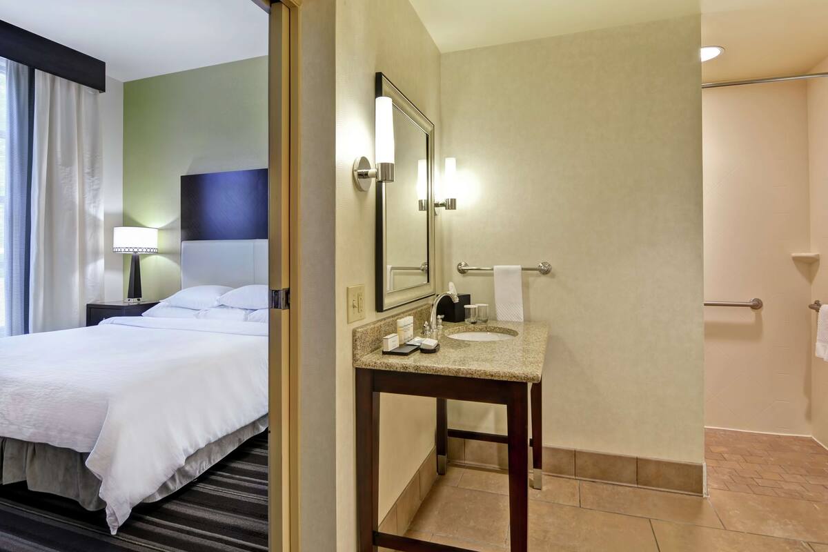 Habitación de hotel con cama, baño con lavabo y espejo, y zona de ducha.