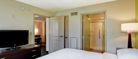 A hotel room with a bed, a TV on a wooden dresser, a lamp, and a door leading to a bathroom.