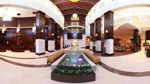 Eine geräumige Lobby mit einem zentralen Wasserspiel, verschiedenen Sitzbereichen und einer hohen Decke mit Holzvertäfelung.