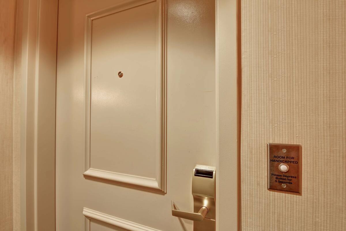 Una puerta con una placa que indica que es una habitación para personas con discapacidad, un timbre y un lector de tarjetas.