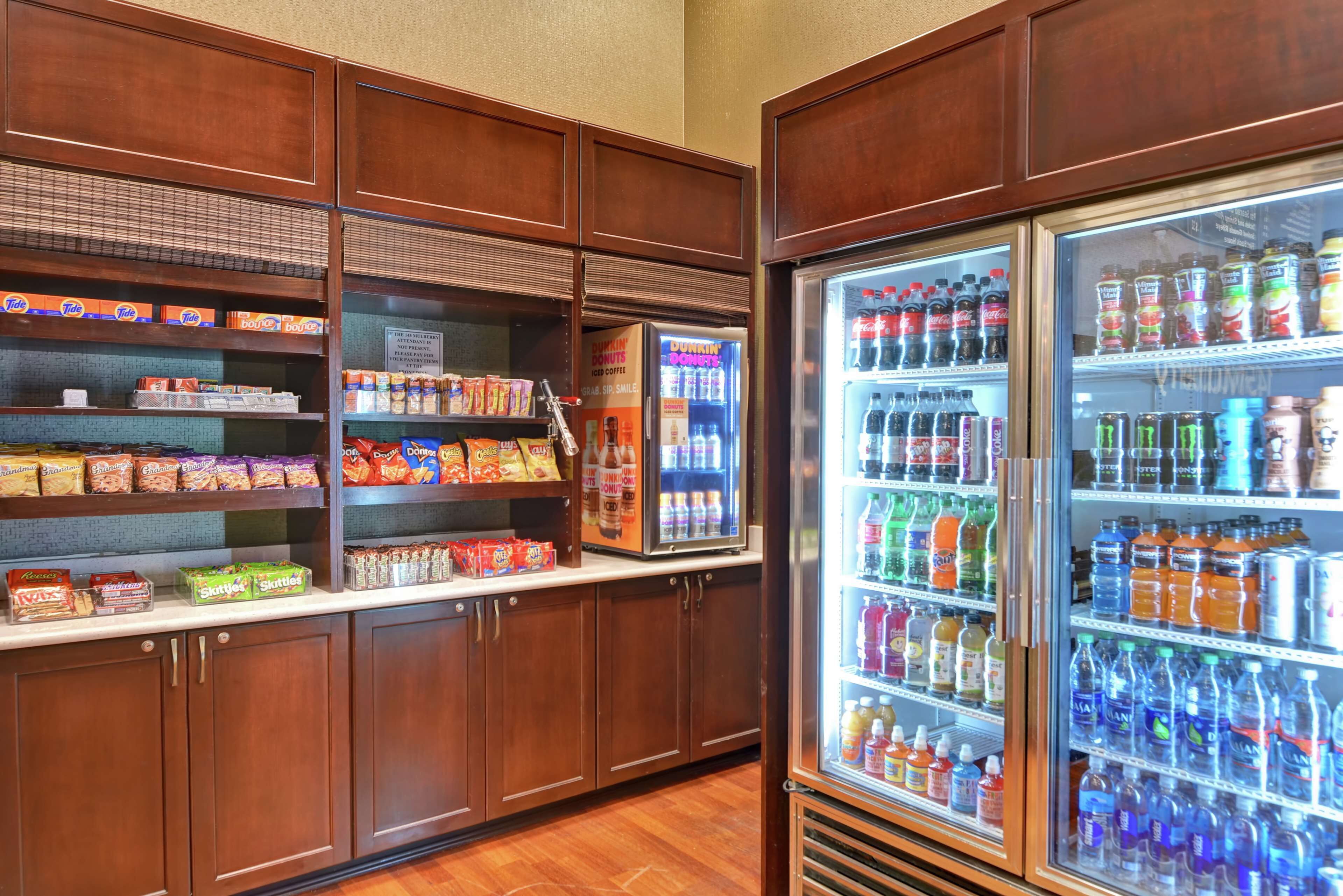 A kitchenette with a refrigerator stocked with beverages and a shelf with snacks.