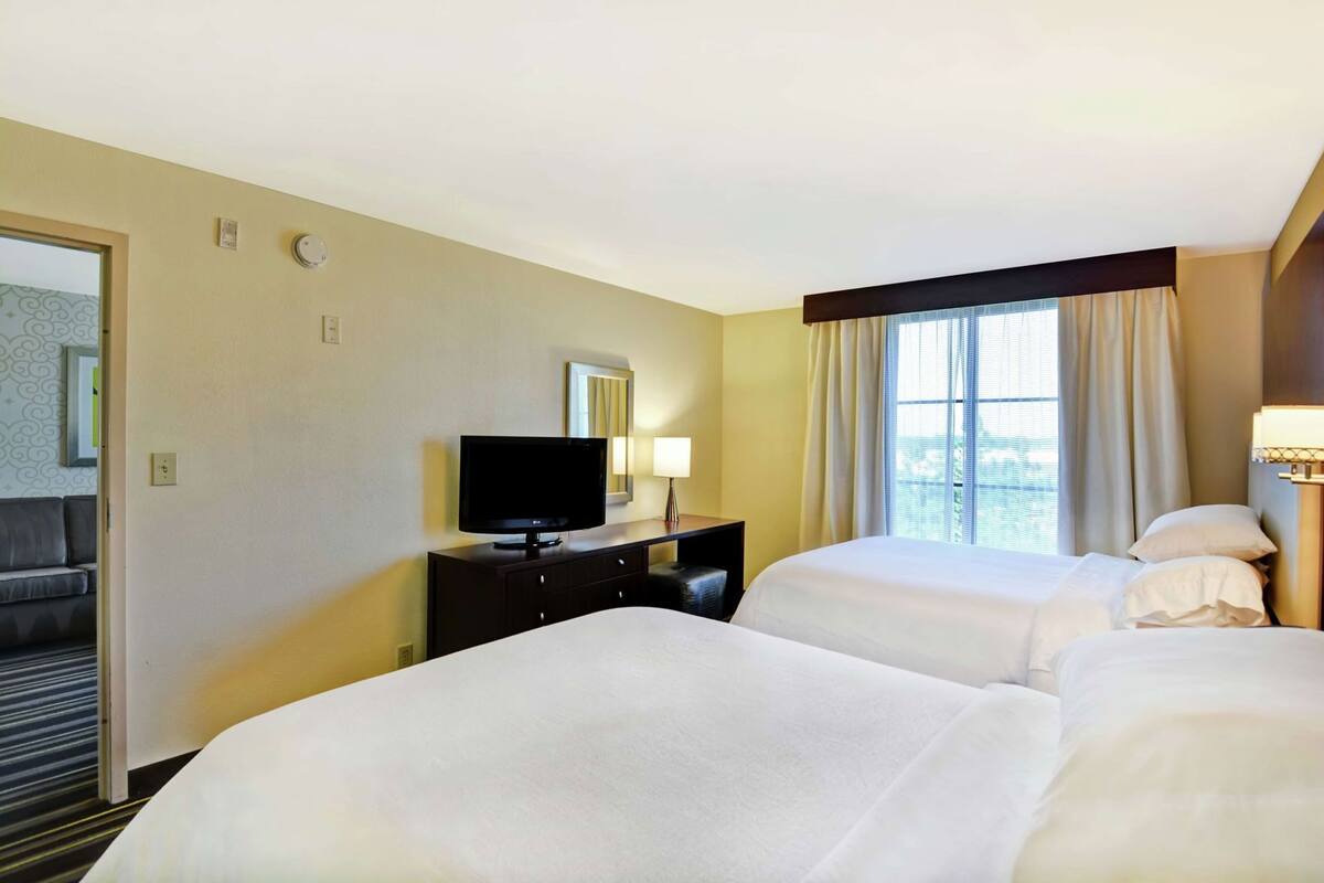 Habitación de hotel con dos camas, televisor, escritorio y ventana con cortinas.