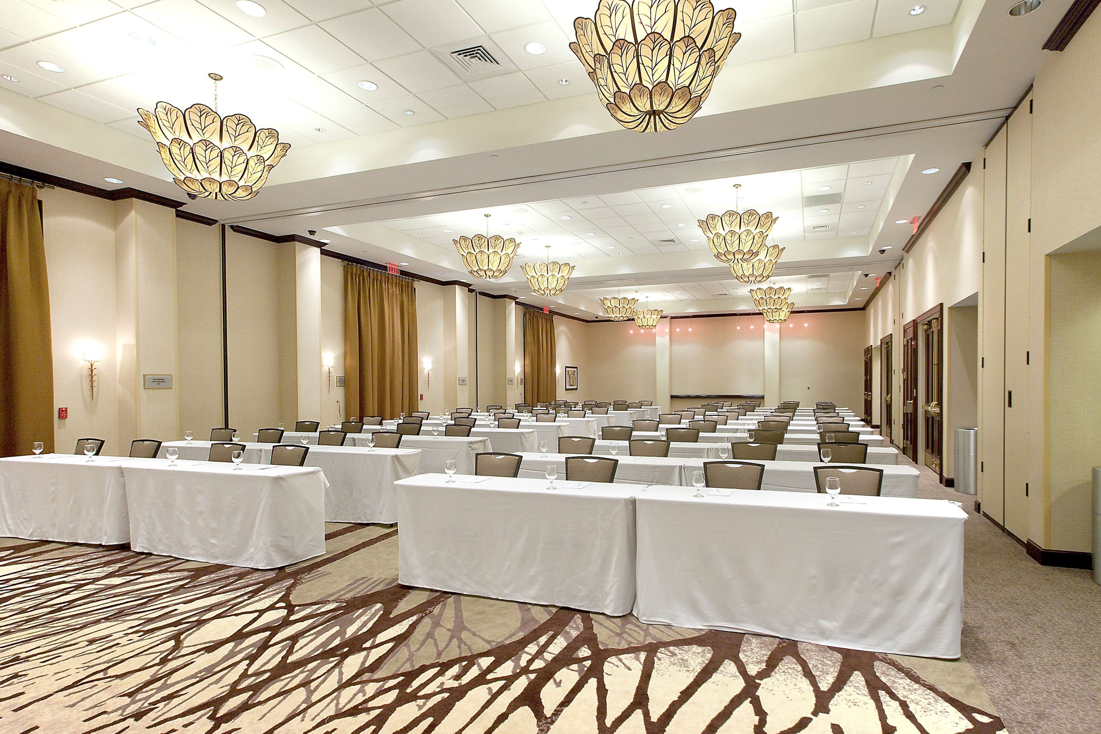 A conference room with rows of tables, chairs, and chandeliers.