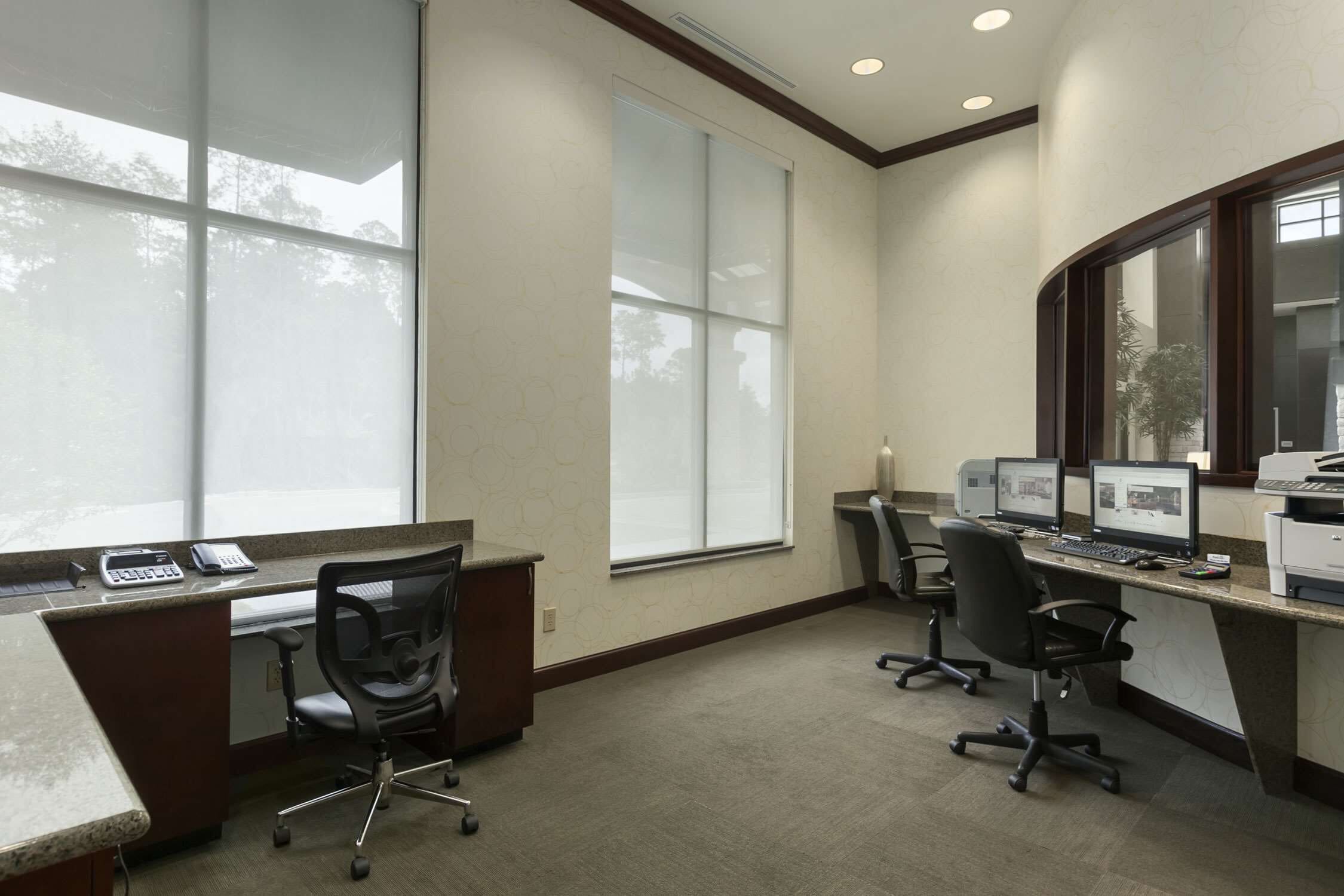 An office with two desks, computers, chairs, and large windows.