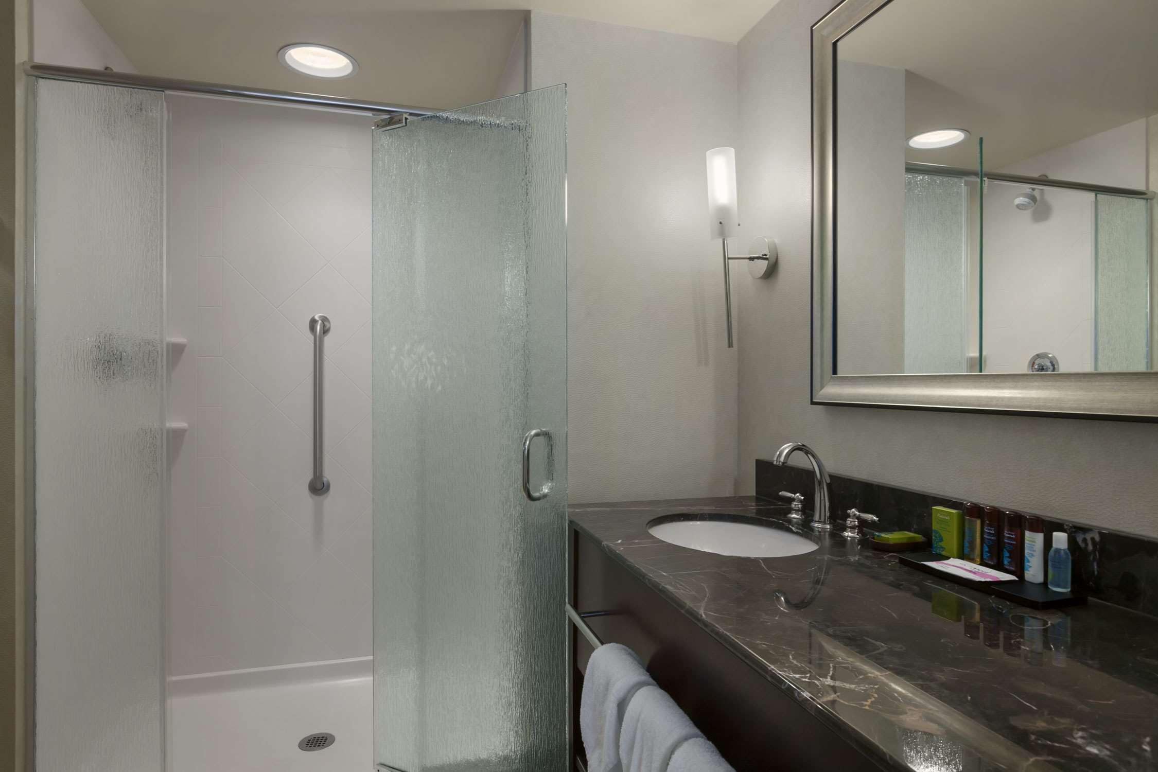 A modern bathroom with a glass-enclosed shower, a marble sink, and a large mirror.
