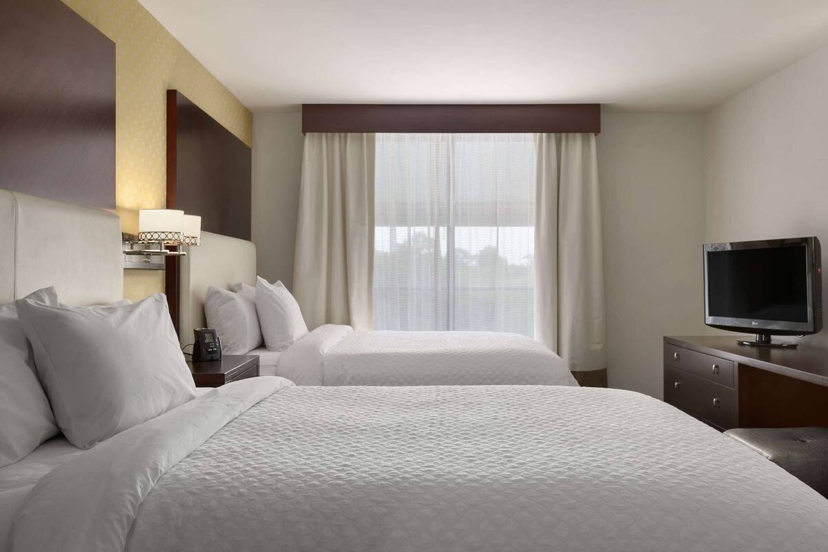 Una habitación de hotel con dos camas, televisión, escritorio y ventana con cortinas.