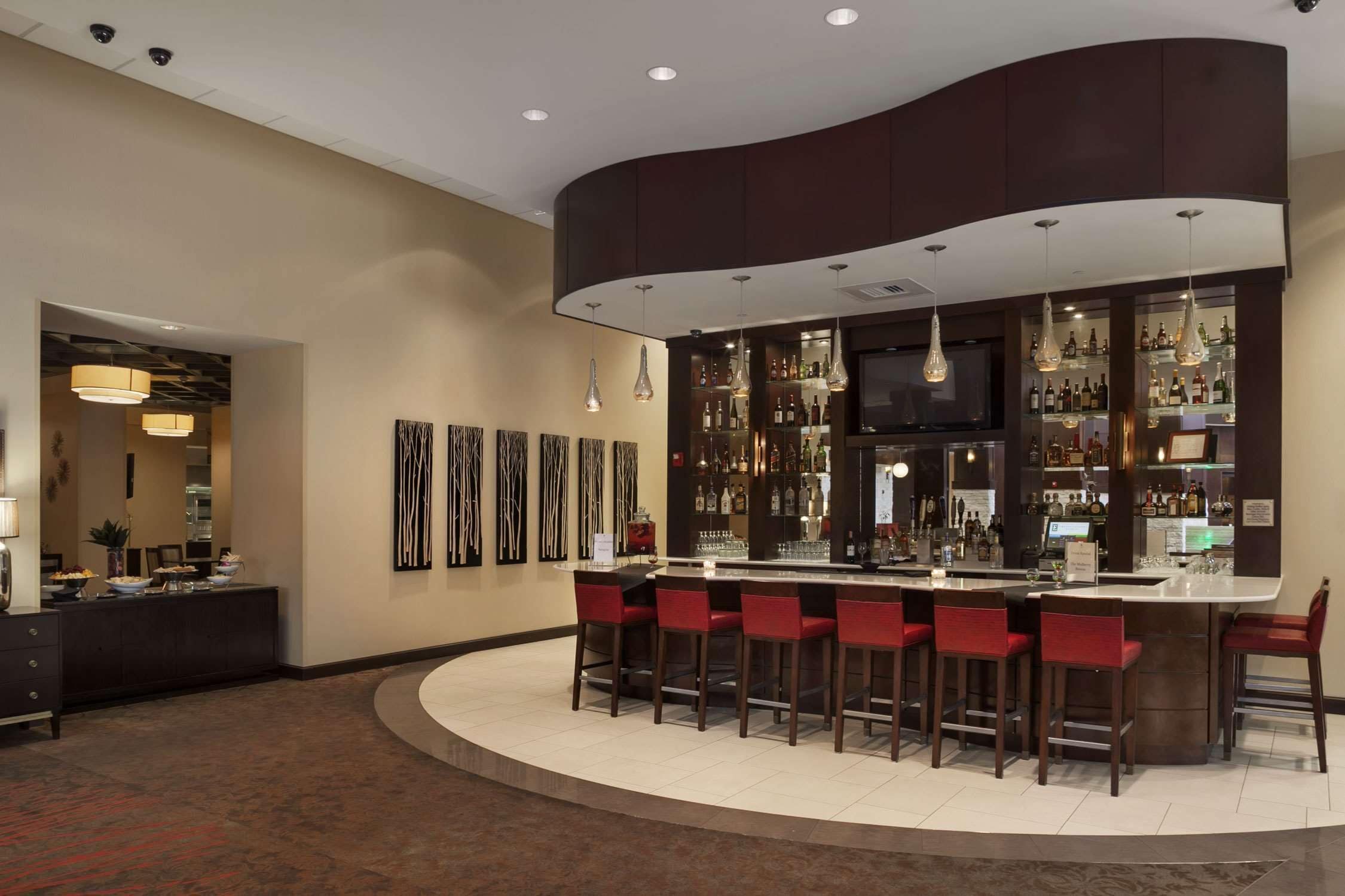 A modern bar area with a curved counter, multiple bar stools, and a variety of bottles and glasses.