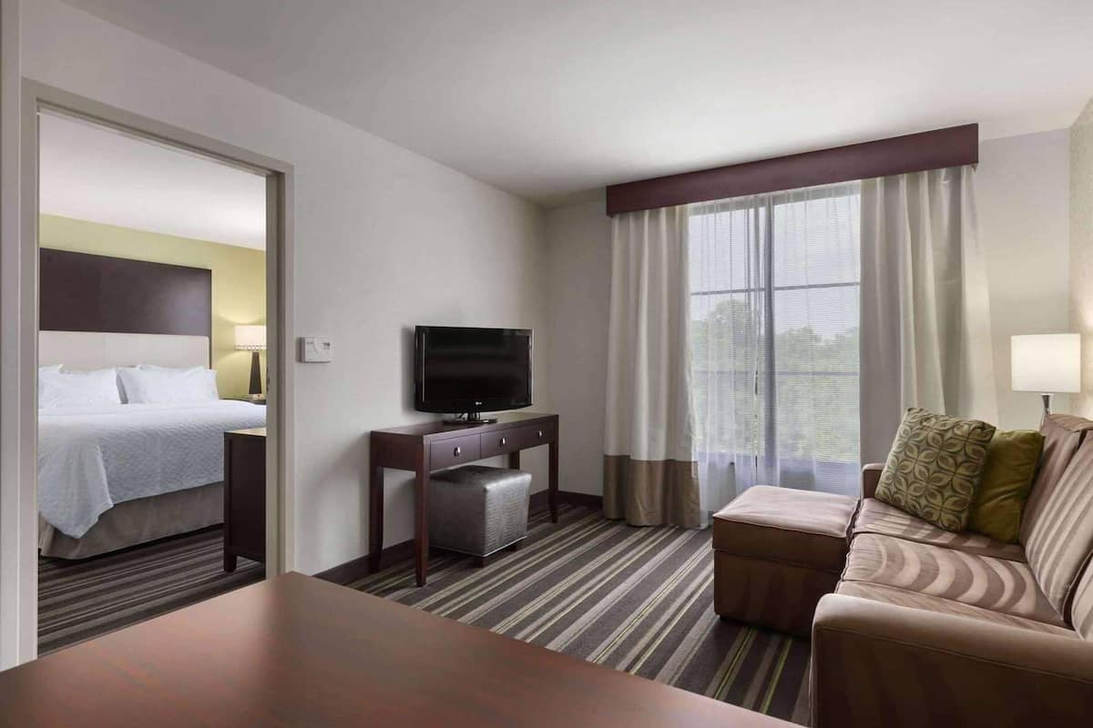 Una habitación de hotel con cama, televisor en un mueble, sofá y mesa de comedor.