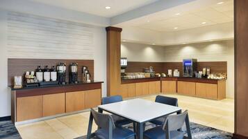 A hotel lobby with a reception desk, a coffee station, and a seating area with a table and chairs.