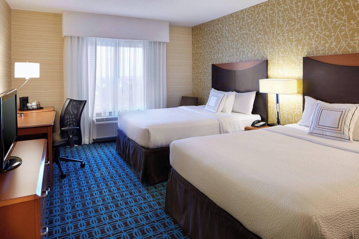 A hotel room with two beds, a desk with a computer, a chair, and a window with curtains.