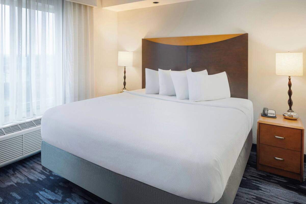A hotel room with a large bed, two bedside lamps, a wooden nightstand, and a window with curtains.