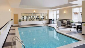 An indoor swimming pool with a glass wall, a seating area with tables and chairs, and a view of the gym area. - Fairfield Inn & Suites Columbus Polaris (Columbus)